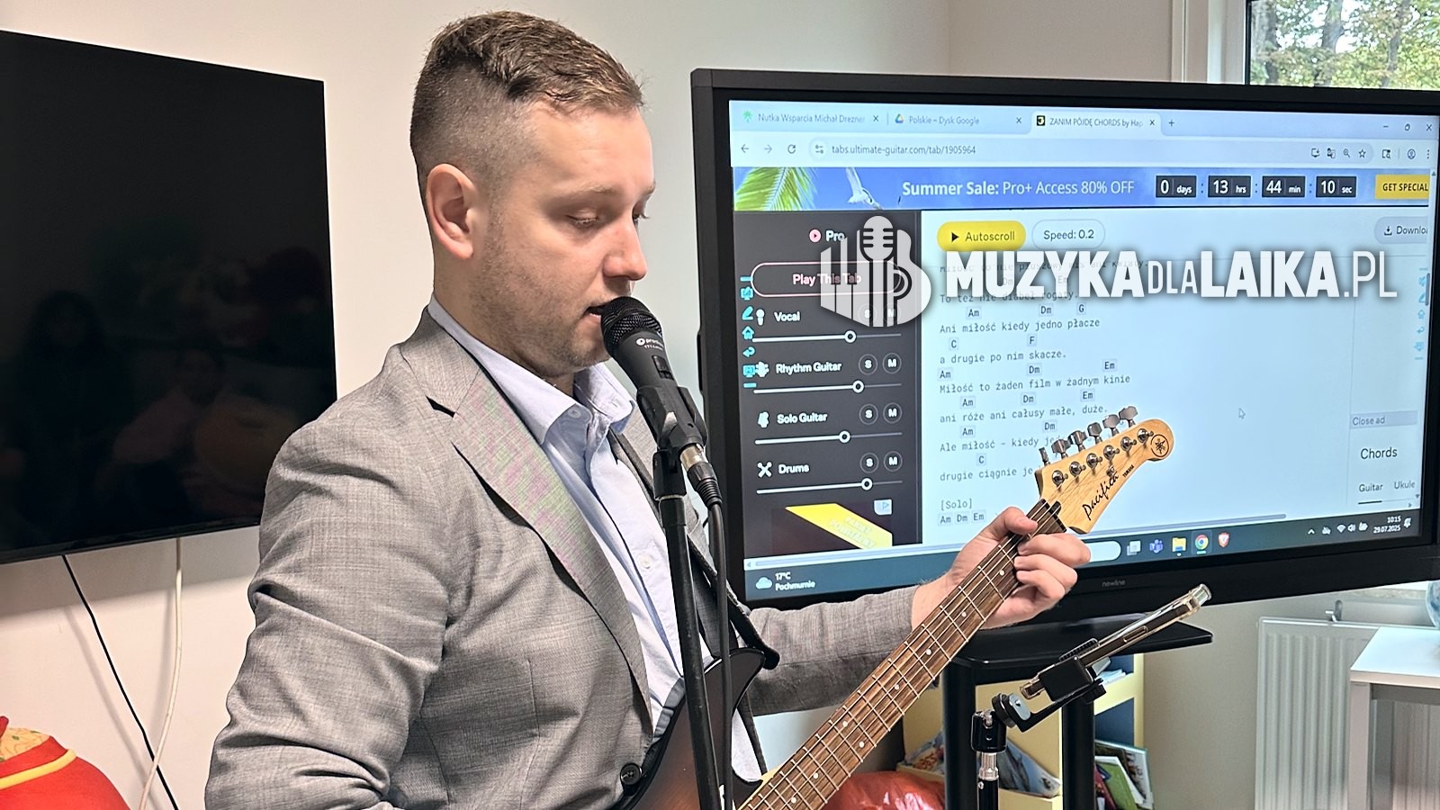 Michał Drezner prowadzi zajęcia z mikrofonem i gitarą przy ekranie