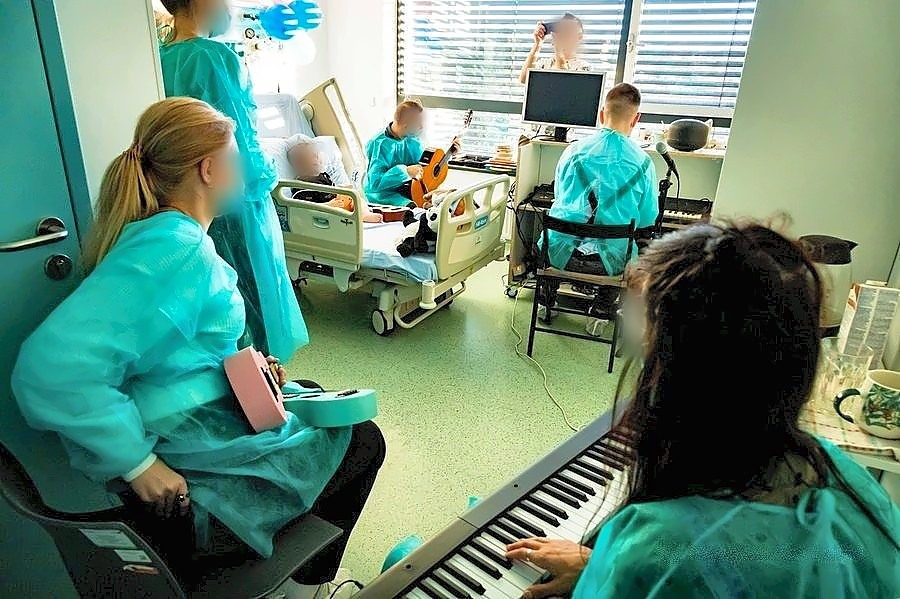 Michał Drezner gra na keyboardzie w sali szpitalnej, obok osoba z gitarą, twarze zasłonięte