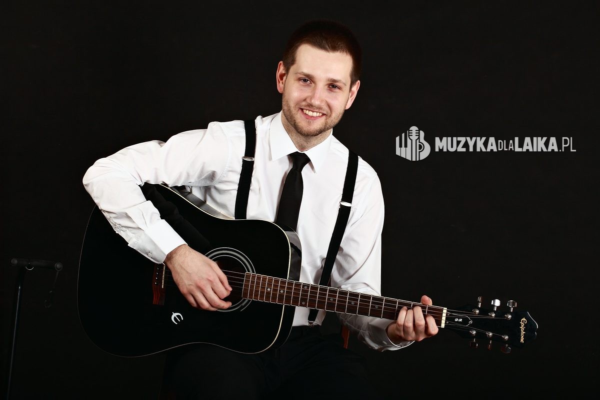 Michał gra na gitarze akustycznej w studiu, na czarnym tle