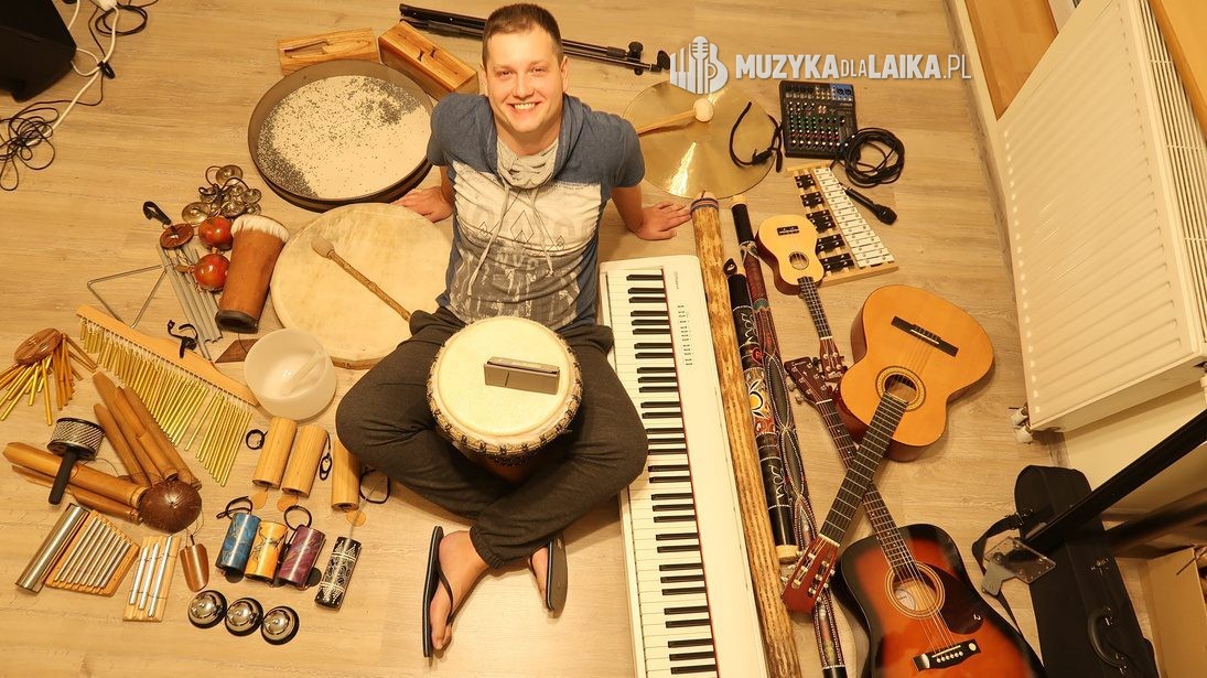 Michał Drezner siedzi na podłodze wśród instrumentów: bębny, grzechotki, dzwonki, gitara i klawisze