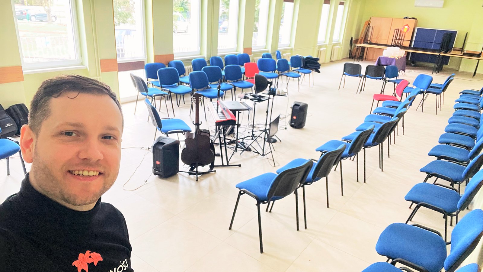 Michał Drezner w sali przygotowanej do wspólnego grania: keyboard, gitara i nagłośnienie, krzesła ustawione dla publiczności.