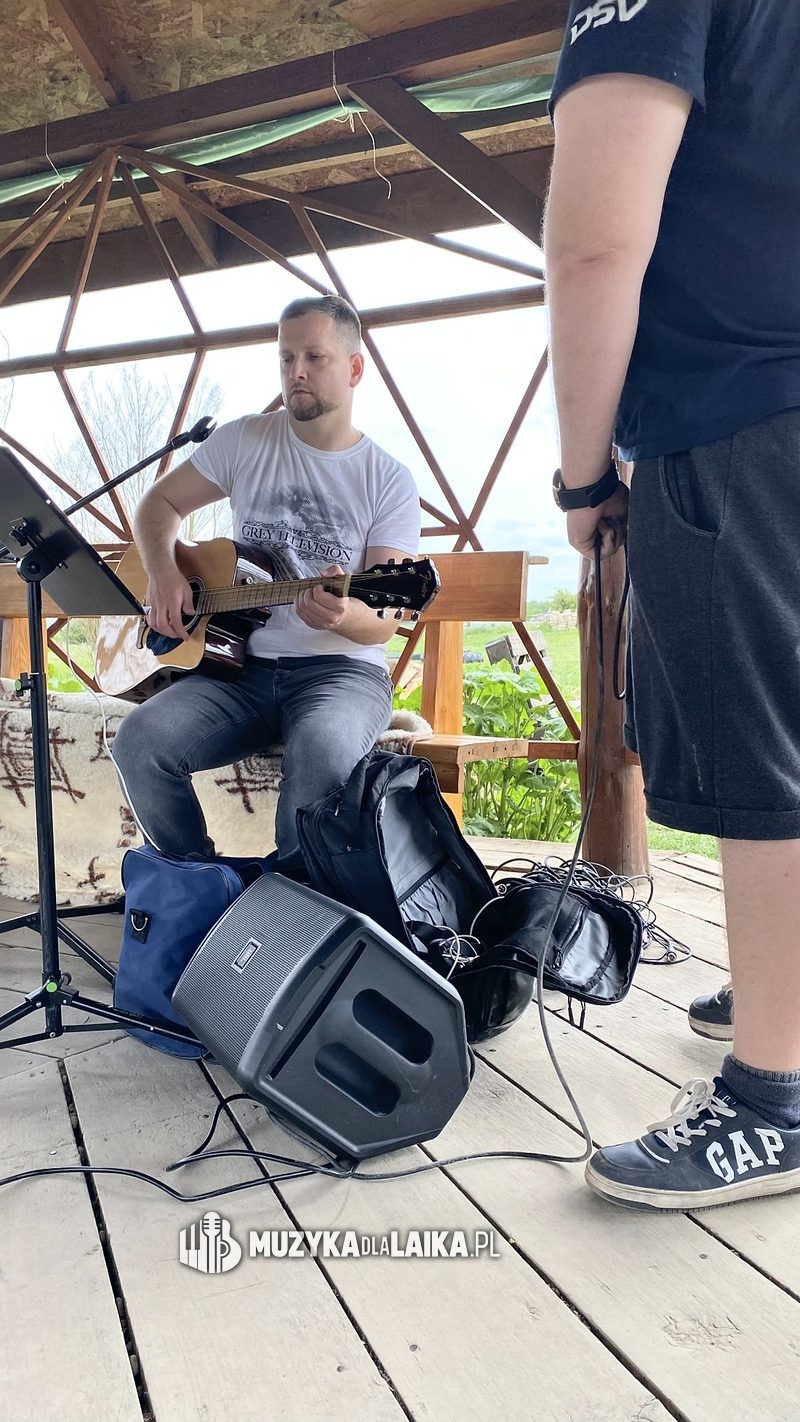 Michał Drezner gra na gitarze w drewnianej altanie