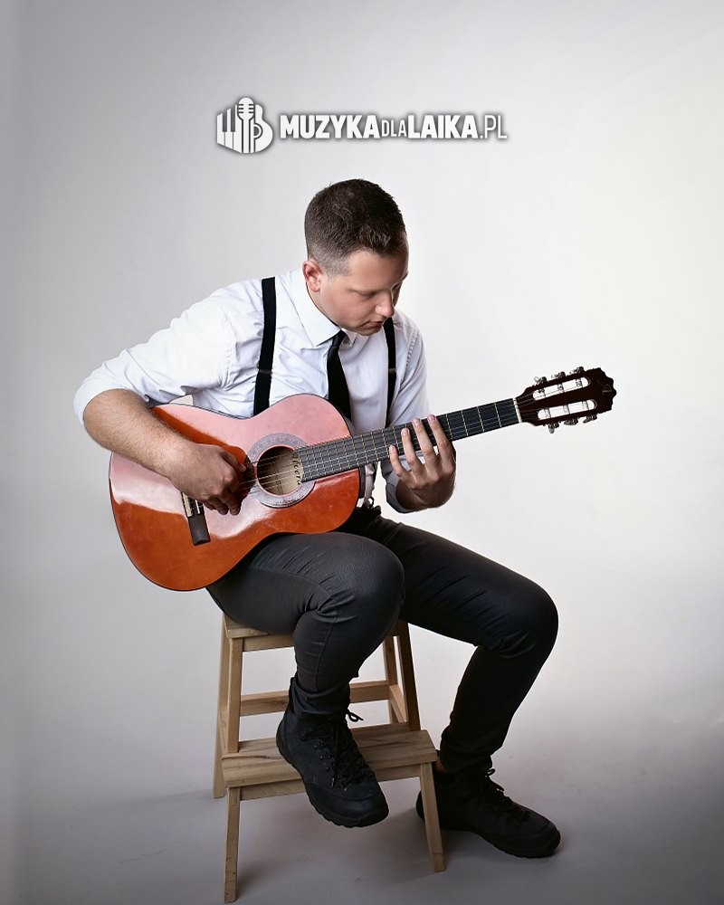 Michał Drezner gra na gitarze klasycznej, siedząc na drewnianym stołku