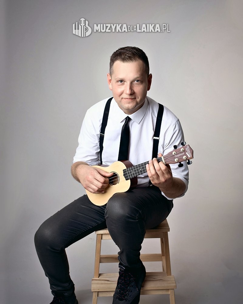 Michał Drezner uśmiechnięty, z ukulele, w białej koszuli i szelkach