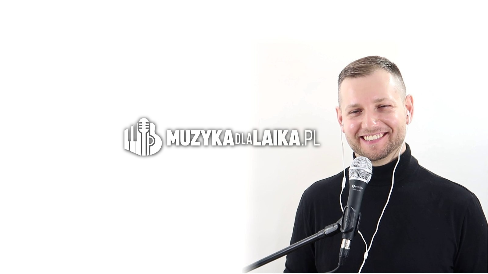 Michał Drezner szeroko uśmiechnięty, w czarnym golfie, przy mikrofonie